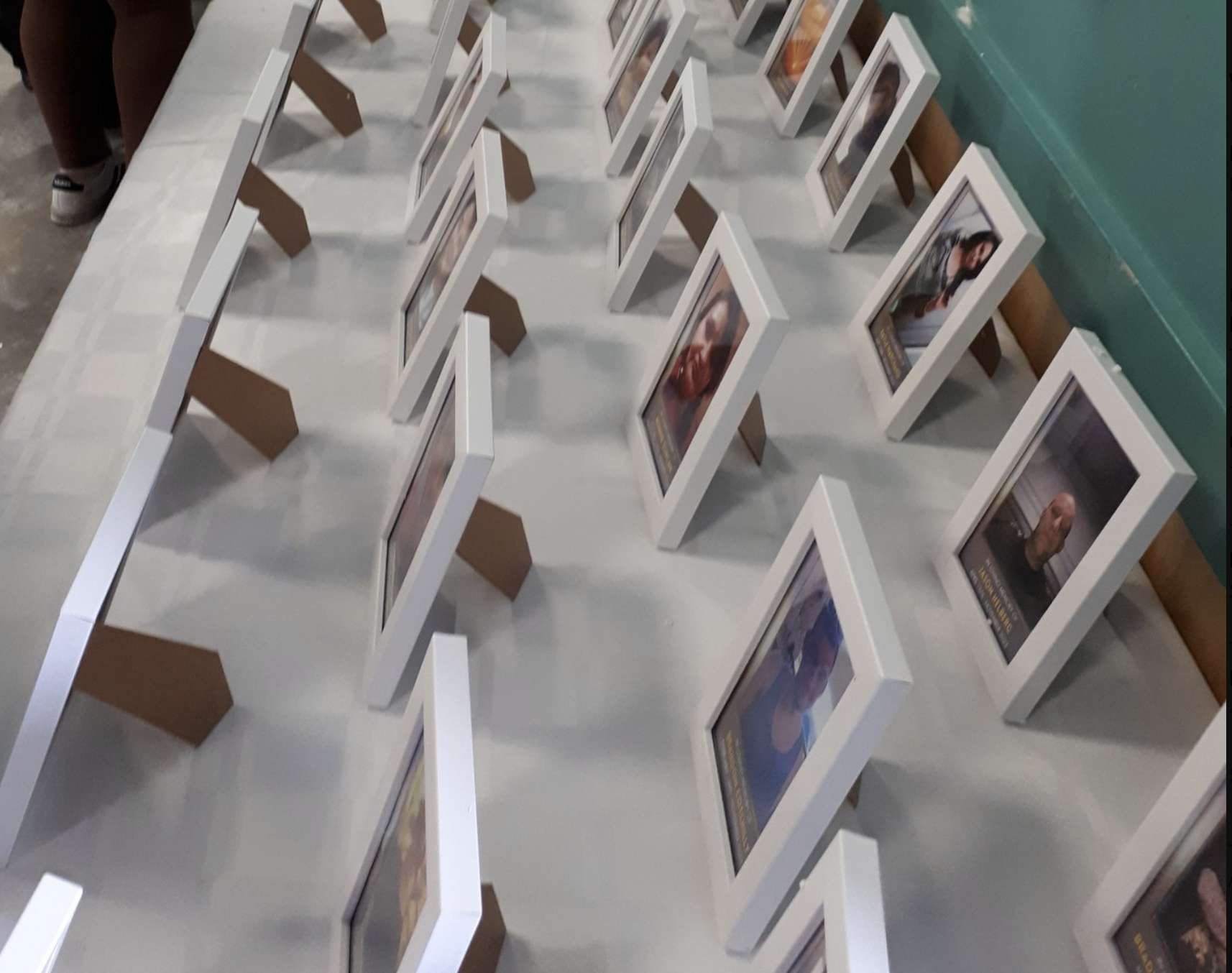 20 photos of people mounted in white frames on a long white table, in 4 rows.