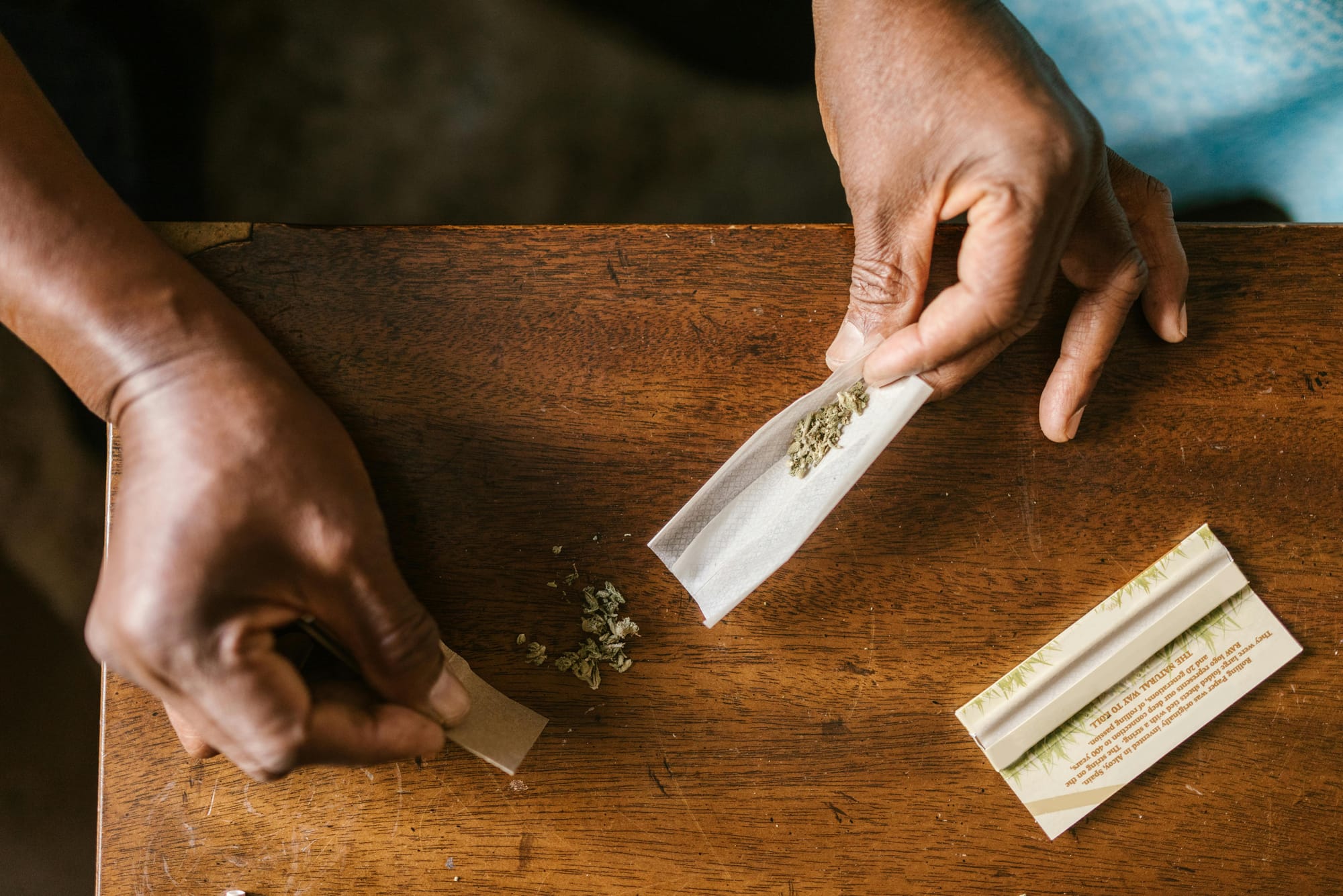 Photo of a person's hands rolling a joint on a wooden table.