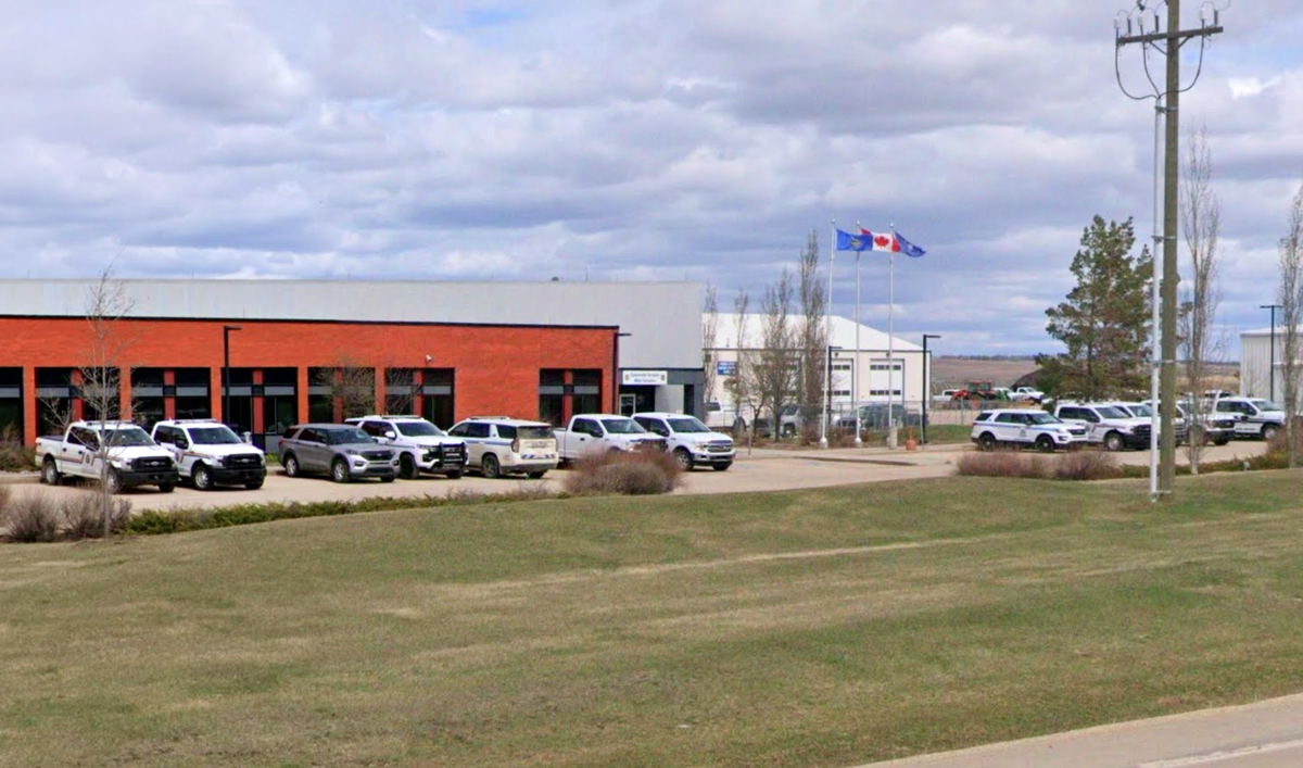 A red brick building with Alberta and Canada flags flying above, and a dozen police vehicles parked in front.