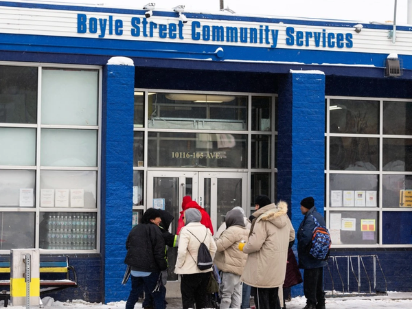 A blue and white painted building in winter with 8 people bundled up standing outside.