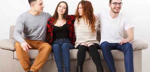 Group of young models with arms around one another on a couch, in staged conversation.