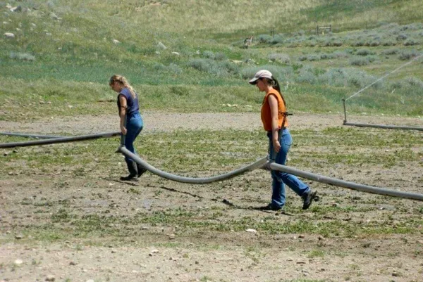 Two youth drag a heavy hose across a field. Their eyes are downcast.