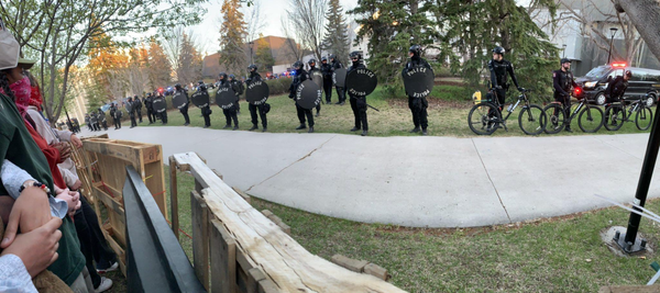 panoramic photograph of police lined up approximately one metre apart in riot gear, behind a sidewalk.