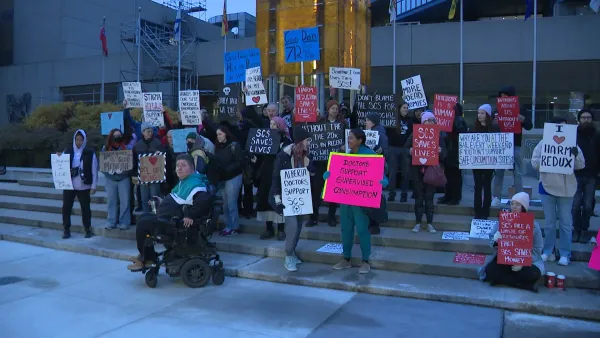 Around 25 people stand with signs on the steps of Calgary City Hall in the early morning.