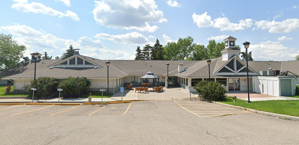 Single-story building in front of a parking lot, with a gazebo and sitting space out front. 