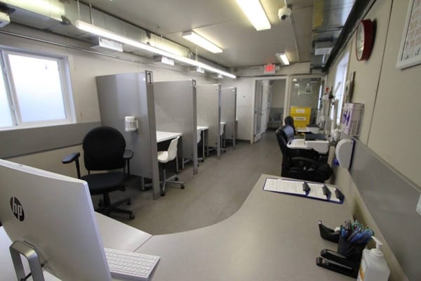 A series of four clean supervised consumption site booths are arrayed along a wall in a small room.