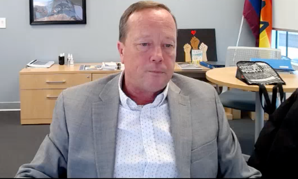 A middle-aged man in a grey suit jacket stares despondently at a downward angle, his mouth set closed.